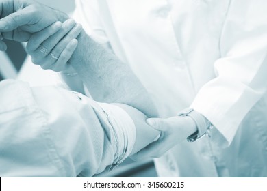 Female Traumatologist Orthopedic Surgeon Doctor Examining Middle Aged Man Patient To Determine Injury, Pain, Mobility And To Diagnose Medical Treatment In Shoulder, Arm, Elbow, Wrist And Fingers.