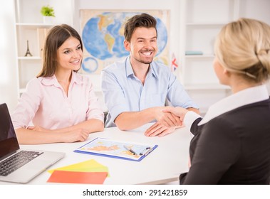 Female Travel Agent Greeting Happy Young Couple At Office.