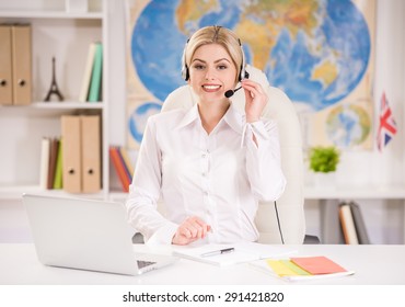 Female Travel Agent Sitting At Office And Talking To Clients With Headset.