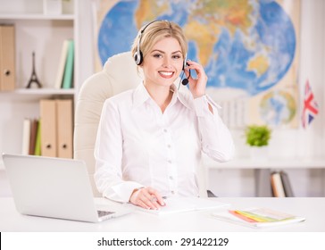 Female Travel Agent Sitting At Office And Talking To Clients With Headset.