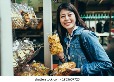 Female Travel Blogger Is Showing A Bag Of Dried Fruit In Front Of Camera. Pretty Korean Woman Buying Healthy Snacks From Metal Rack Is Smiling. 