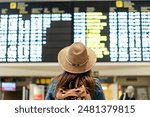 Female traveler in airport terminal looking at flight departures on the light panel