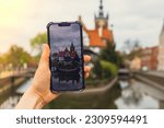 Female traveler in historical places courtyard of landmark and shoots short video on phone. Tourist photographs historic place on sunny day in Gdansk Poland. Unrecognizable woman Tourism and blogging