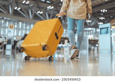 Female traveler passenger walking with a yellow suitcase at the modern Airport Terminal, Back view of woman on her way to flight boarding gate, Ready for travel or vacation journey	