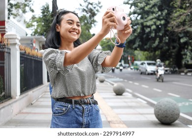 Female traveler with pink picture camera Instax capturing moment of the city