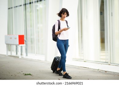 Female Traveler Pulling Rolling Suitcase And Text Messaging On Mobile Phone In City