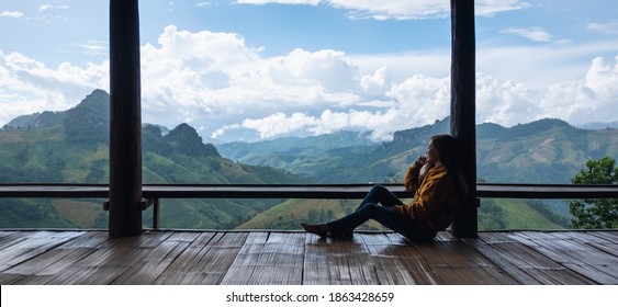 A female traveler sitting and looking at a beautiful mountains and nature view on wooden balcony
