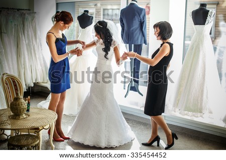 Female trying on wedding dress in a shop with two women assistants.