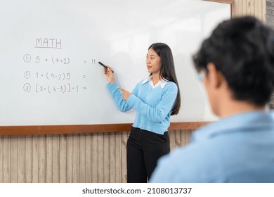 Female Tutor Standing In Front Of Whiteboard And Writing Math Equations On Board To Explaining For Student During Math Class In The Classroom