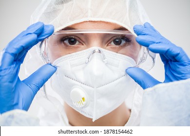 Female UK Doctor,nurse Or Lab Tech Virology Scientist In PPE,putting On Protective Eyewear Goggles,wearing Blue Latex Gloves,white FFP2 Face Mask,closeup Headshot Portrait Isolated On White Background