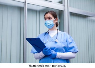 Female UK ICU medical worker,woman doctor holding clipboard wearing PPE blue protective scrubs face mask,front line emergency medic,COVID-19 pandemic crisis,Coronavirus patient quarantine triage  - Powered by Shutterstock