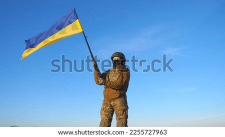 Female ukrainian army soldier holding waving flag of Ukraine. Woman in military uniform and helmet lifted up flag against blue sky. Victory against Russian aggression. Invasion resistance concept.
