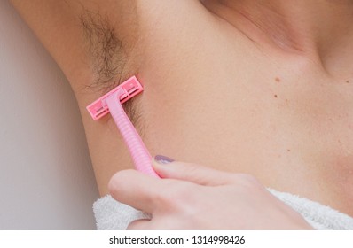 Female unshaved armpits or woman with long hair underarm, depilation, hair removal concept. Young woman shaves hairy armpits with a disposable razor.  Close-up, selective focus.