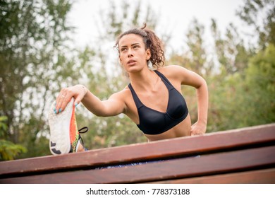 Female urban runner warming up and stretching her leg on wooden bench. - Powered by Shutterstock