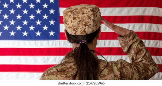 Female US Army Soldier Standing In Front Of An American Flag And Saluting. Woman In Military Uniform Rear View