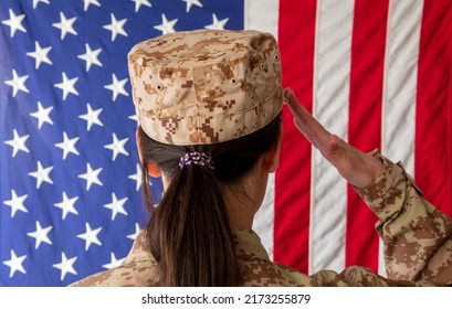 Female US Army Soldier Standing In Front Of An American Flag And Saluting. Woman In Military Uniform Rear View