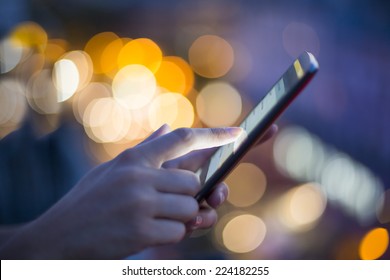 Female using her mobile phone, city skyline night light  background - Powered by Shutterstock