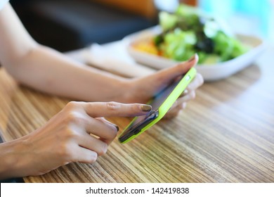 Female Using Mobile Phone On Food Table