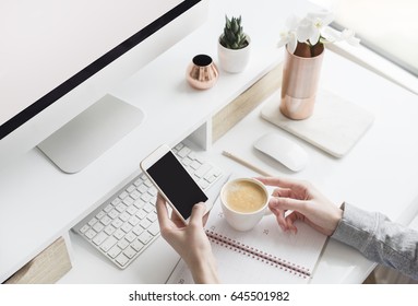  Female using mobile smart phone while having coffee break. White desk. Workspace