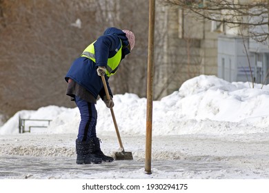 A Female Utility Worker Clears Snow From The Sidewalk