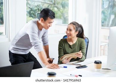 Female UX Designer Showing Her Work On Tablet Computer To Smiling Coworker