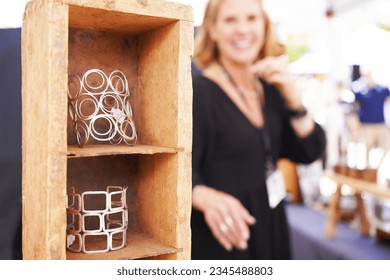 Female vendor at a crafts fair in her booth selling handmade artisan jewelry, looking at the tower of bracelets and smiling in the background - Powered by Shutterstock