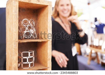 Female vendor at a crafts fair in her booth selling handmade artisan jewelry, looking at the tower of bracelets and smiling in the background