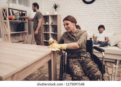 Female Veteran In A Wheelchair Is Cleaning House. Supporting Husband. Camouflage Uniform. Disabled Soldier. Family Concept. Working Together. Holiday Leisure. Yellow Gloves. Free Time.