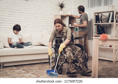 Female Veteran In A Wheelchair Is Cleaning House. Supporting Husband. Camouflage Uniform. Disabled Soldier. Family Concept. Working Together. Holiday Leisure. Yellow Gloves. Free Time.