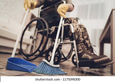 Female Veteran In A Wheelchair Is Cleaning House. Broom And Scoop. Camouflage Uniform. Disabled Soldier. Floor Sweeping. Working Together. Holiday Leisure. Yellow Gloves. Free Time.