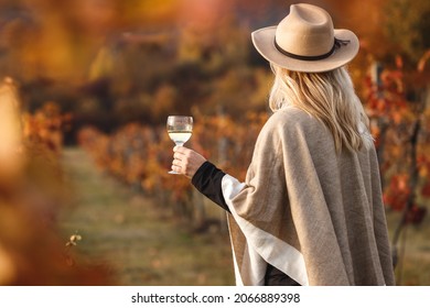 Female vintner enjoying white wine in her vineyard. Woman with poncho and hat holding glass of wine outdoors. Winery at autumn - Powered by Shutterstock