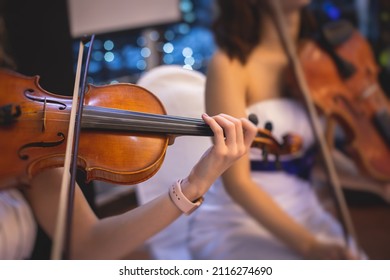 Female violin player, fiddler violinist with a bow performing music on stage during concert with orchestra and musical band in the background