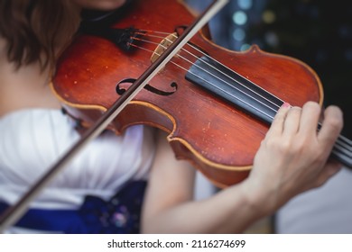 Female Violin Player, Fiddler Violinist With A Bow Performing Music On Stage During Concert With Orchestra And Musical Band In The Background