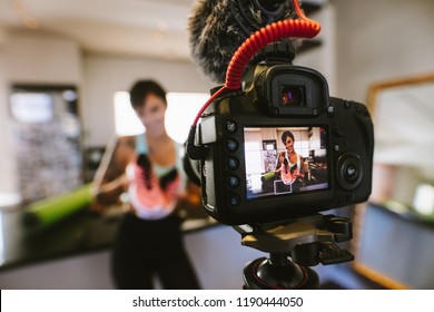 Female vlogger holding sports shoes in hands happily looking in camera while recording video for blog. Focus on camera with social media influencer reviewing and marketing a sports shoe.