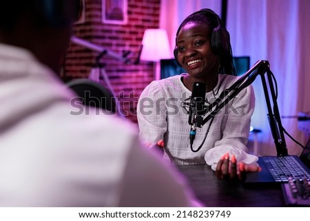 Female vlogger interviewing male guest on podcast show, using recording equipment. Happy woman streaming live broadcast episode with man in studio to record conversation for channel.