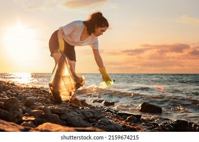 A female volunteer is collecting plastic garbage on the seashore. Cleaning of the coastal zone. Copy space. The concept of Earth Day and environmental conservation. - Powered by Shutterstock