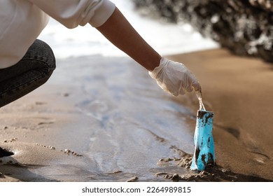 Female volunteer picking up used disposable medical face masks on the beach, cleaning coastal zone, closeup. The environmental problem after the coronavirus pandemic - Powered by Shutterstock