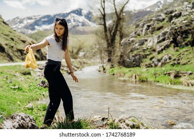 Female volunteer walking along river bank, picking up litter.Cleaning nature from plastic waste.Active responsible woman volunteering for cleaning up trash from riverbed,prevent water pollution - Powered by Shutterstock