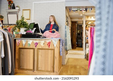 Female Volunteer Working In Charity Shop Or Thrift Store Selling Used And Sustainable Clothing And Household Goods