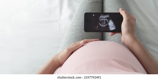 Female waiting her baby, Pregnant woman looking her ultrasound scan photo on Smartphone. Concept of pregnancy, Maternity prenatal care. - Powered by Shutterstock