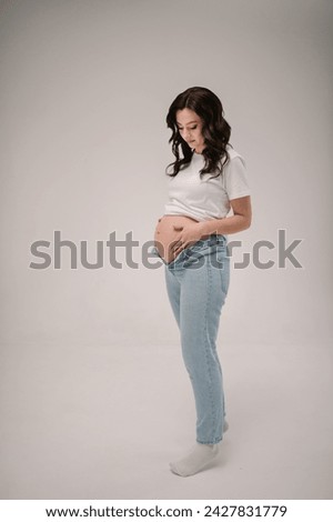 Female waiting for newborn baby on white background. Pregnancy motherhood procreation concept. Belly of a pregnant woman. Young pregnant girl touching and holding belly and caring about health indoors