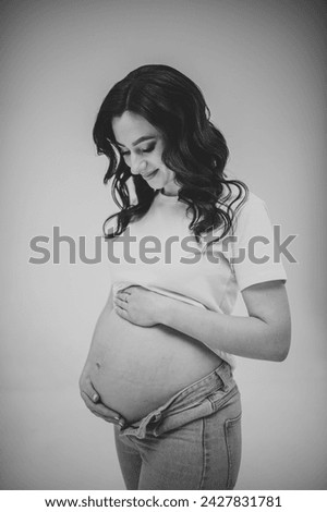 Female waiting for newborn baby on white background. Young pregnant girl holding belly and caring about health. Pregnancy motherhood procreation concept. Belly of pregnant woman. Black and white photo