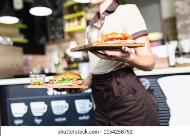 Female waitress is carrying two plates with sandwiches.