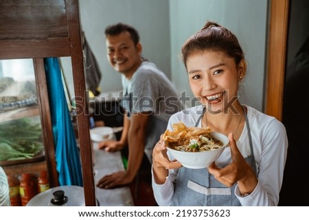 female waitress smiling while bringing a bowl of chicken noodles for customers in a stall cart