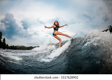 Female wakesurfer in black swimsuit makes dangerous stunts on a green and orange board