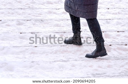 Female walks up stairs with snow steps during snowfall. Woman climbs snow covered staircase. Person climbing slippery snowy stairs. Dangerous winter walking. Selective Focus
