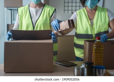 Female Warehouse Coworkers Preparing Food Delivery Boxes While Wearing Safety Mask For Coronavirus Prevention - Main Focus On Center Hand