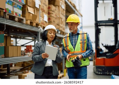 Female warehouse manager and a worker cooperating while using digital tablet in storage room. 