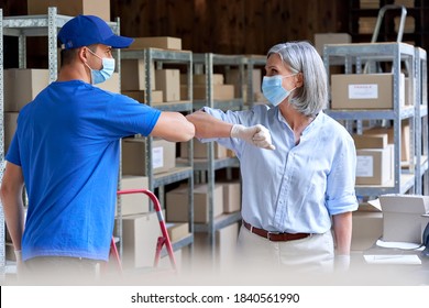 Female Warehouse Worker Manager Wearing Face Mask Greeting Male Courier Deliverer Giving Elbow Bump Standing In Post Shipping Delivery Storage. Covid 19 Healthcare Protection Social Distance At Work.