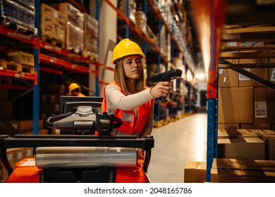 Female warehouse worker with safety helmet is working with bar code scanner while sitting on forklift in warehouse - Shutterstock ID 2048165786